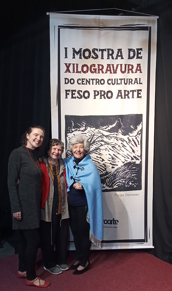 Noni Ostrower entre as curadoras da mostra, Silviane Lopes (à esquerda) e Izadora Andrade. No banner, obra de Fayga Ost